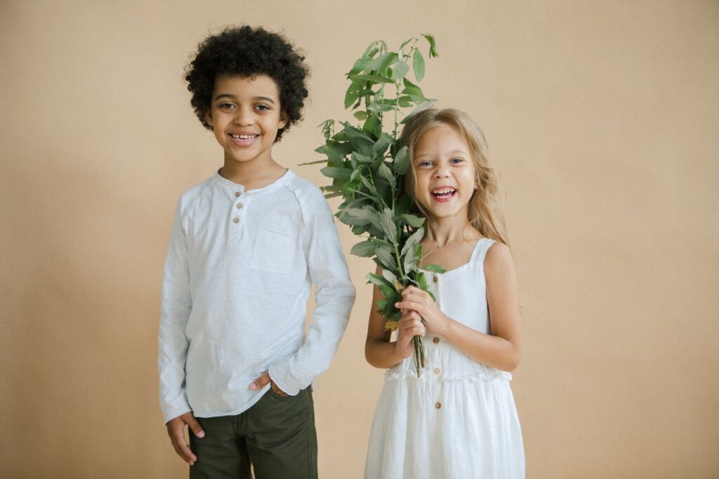 Smiling children posing happily with fresh green plant against a neutral background.